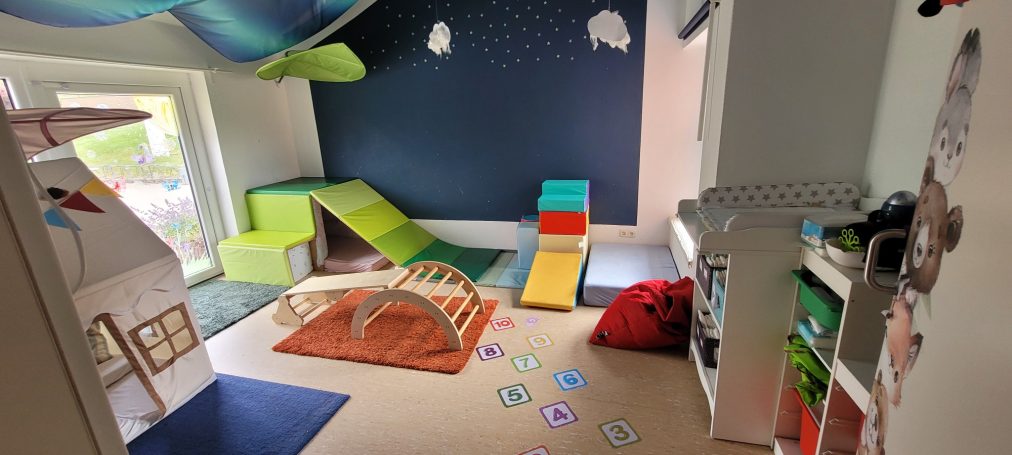 Bunt eingerichteter Spielraum mit Spielgeräten, Teppich und Fensterlicht.
